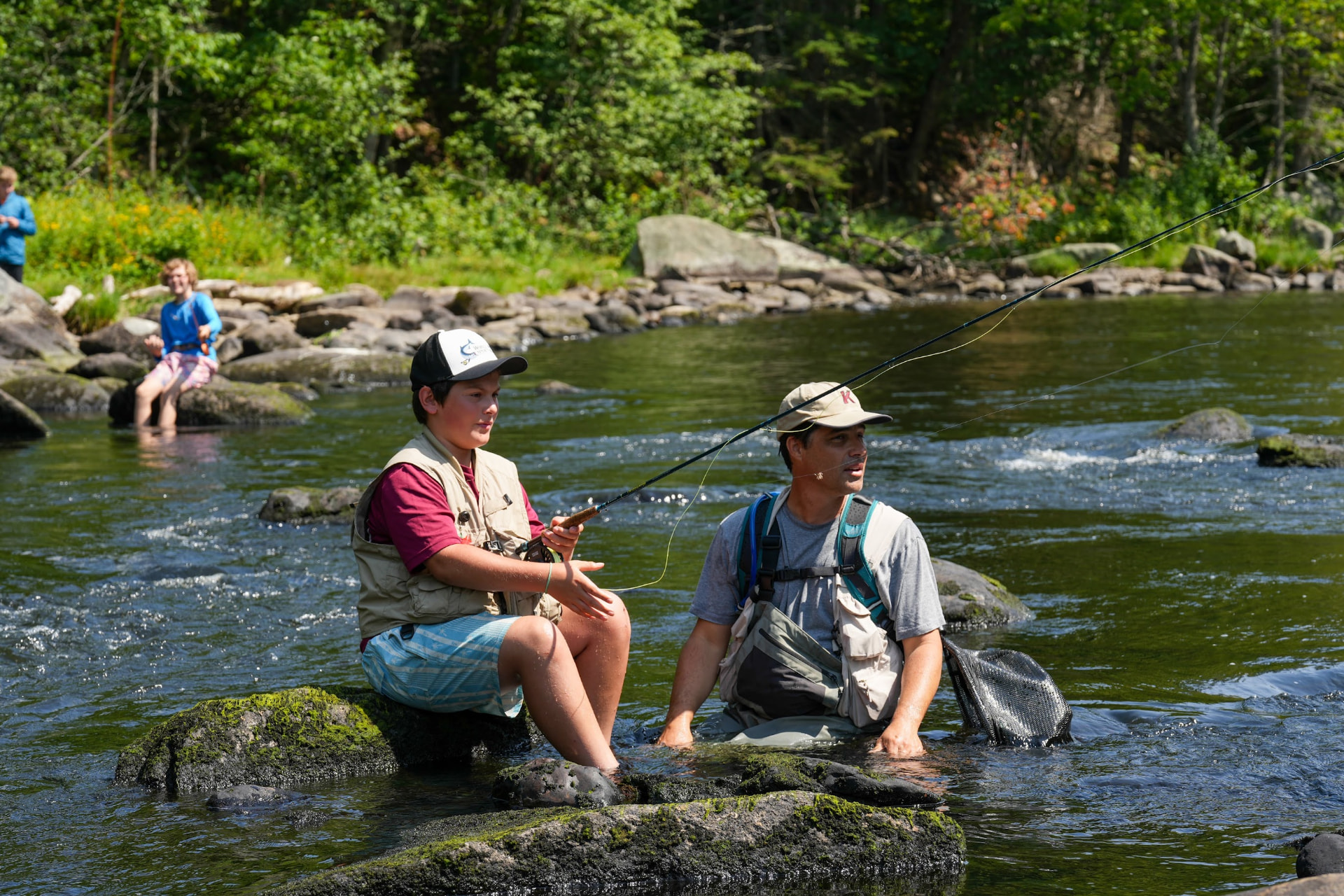 Kevin Bonasera teaching fly fishing to a camper on the rocks at Camp Kawanhee